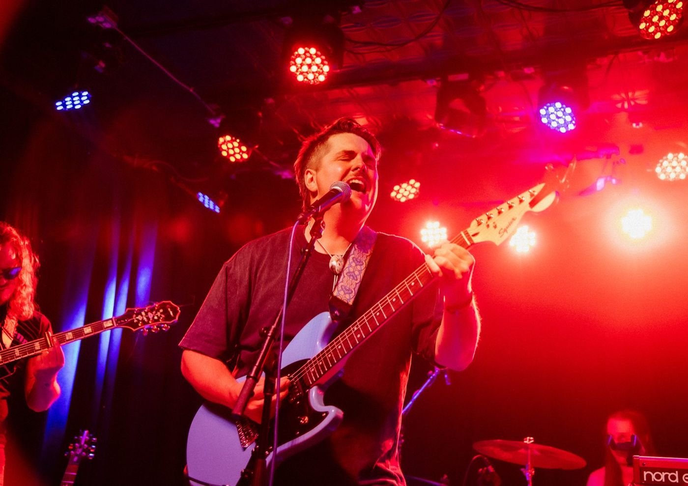 Jake Black singing with electric guitar on a club stage under red lights